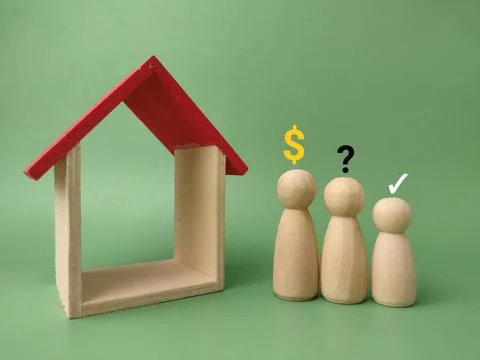 Three wooden figures stand by an empty house frame with a red roof under a .. 库存照片