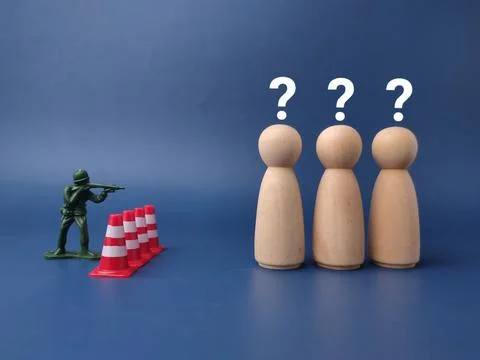 Three wooden peg dolls with question marks above stand opposite a green toy.. Stock Photos