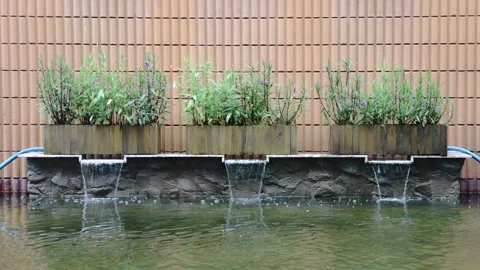Three wooden planter boxes over a stone base. Water cascades into a clear p.. Stock Footage 339050331