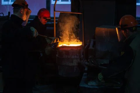 Three workers with ladle prepairing to pour molten steel into mold Stock Photos