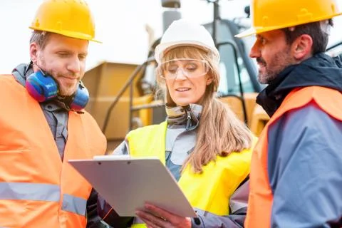 Three workers in a quarry discussing in front of heavy machinery Stock Photos