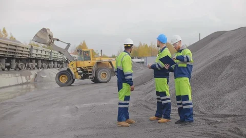 Three workers in a quarry discussing standing on construction site and looking Stock Footage 124070161