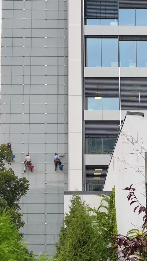 Three workers in work attire are focused on washing windows on a skyscraper. Stock Footage 252001706