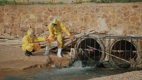 Three workers in yellow hazmat suits inspect an outflow pipe Stock Footage 343334100