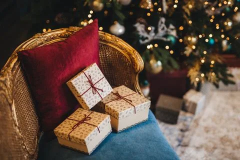 Three wrapped present boxes on armchair near Christmas fir tree. Design or .. Stock Photos