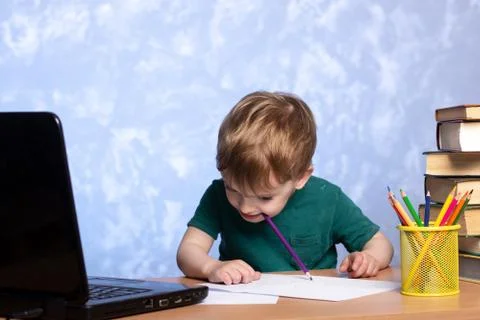 A three year old boy bowed his head over his desk and nibbles a pencil. Foto stock