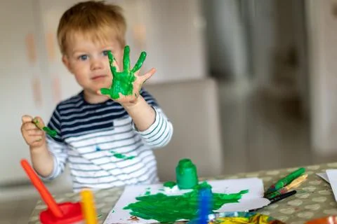 Three year old boy busy painting at home, with paint pots and brushes. Stock Photos