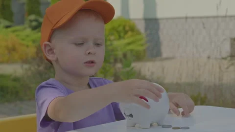 Three year old boy collect coins in piggy bank in home garden 1 Stock Footage 277076680