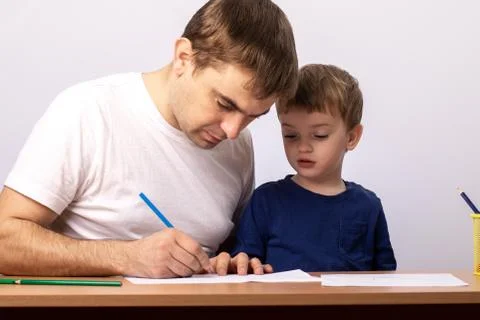 A three-year-old boy with dad sits at a table with books learning to write Stock Photos