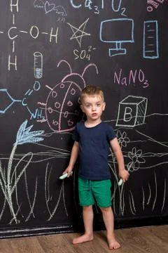 Three year old boy draws with colorful chalk on a large blackboard. Stock Photos