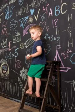 Three-year-old boy draws with multi-colored chalk on a large blackboard. Stock Photos