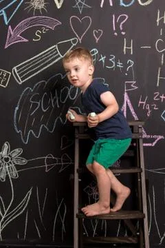Three-year-old boy draws with multi-colored chalk on a large blackboard. Foto stock