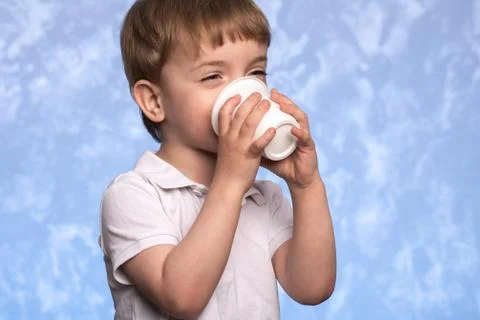 A three-year-old boy drinks water from a disposable cornstarch cup. Stock Photos