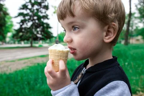 Three year old boy eating ice cream in a waffle cup in a park Stock Photos