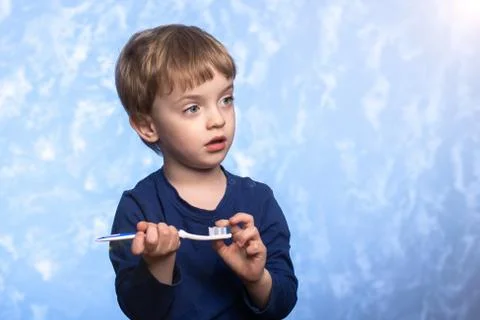 A three-year-old boy holds a plastic toothbrush in his hands. Stock Photos