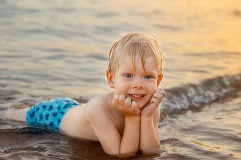 A three year old boy lying in shallow sea water Stock Photos