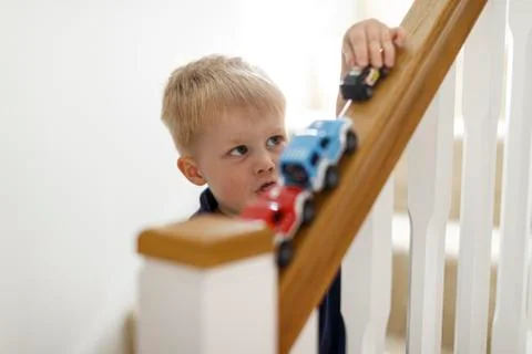 A three year old boy playing with his toy cars on the stair bannister. Stock Photos