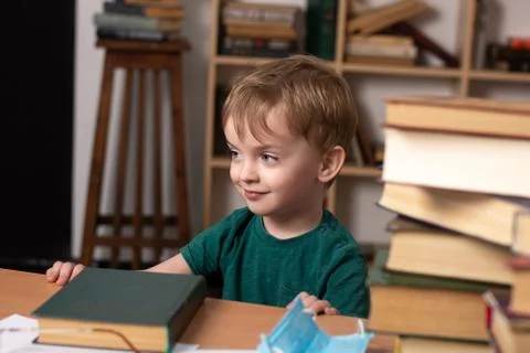 A three-year-old boy sits at a desk with books. Stock Photos