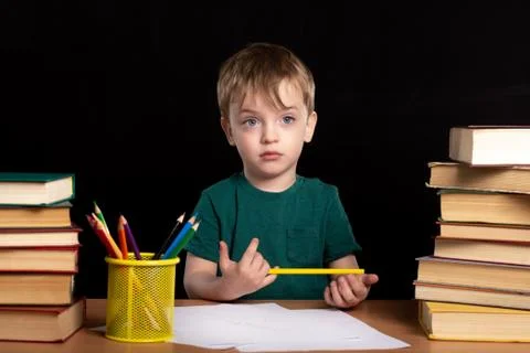 A three-year-old boy sits with a pencil in his hand at the table Stock Photos