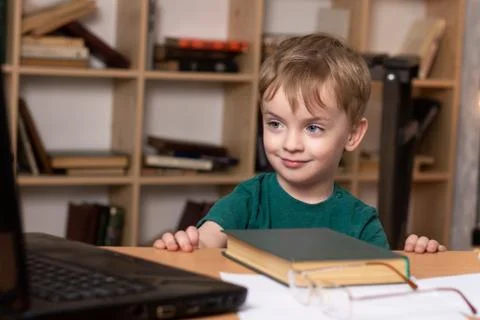 A three year old boy sits at a table and watches online lessons. Stock Photos