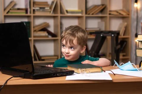 Three-year-old boy sits at the table looks at the laptop monitor. Foto stock