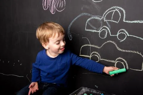 A three year old child draws in chalk on a slate wall of a typewriter Stock Photos