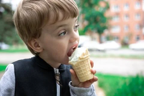 Three year old child eats ice cream in the park on a background of green trees. Stock Photos