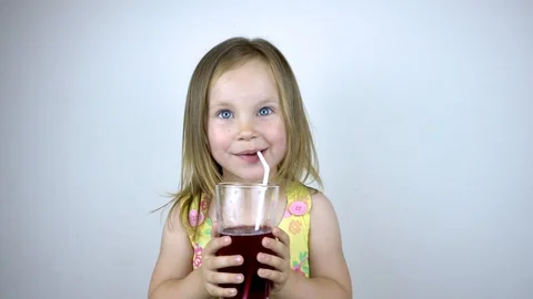 A three year old child girl drinks juice from a glass cup with a straw. On a Stock Footage 113142953