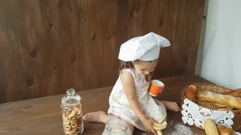 A three-year-old girl in a white dress  eats a large bagel and drinks with juice Stock Footage 157126487