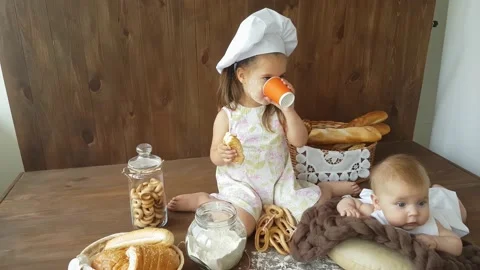 A three-year-old girl in a white dress  eats a large bagel and drinks with juice Stock Footage 157126492