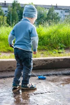 A three-year-old white boy in a blue hat, jeans and sandals plays on a cool Stock Photos