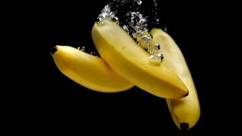 Three yellow bananas falling into transparent water on black background Stock Footage 108783947
