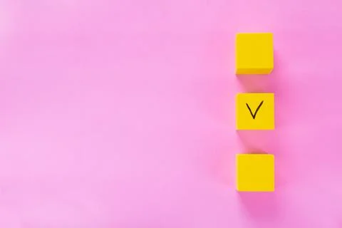 Three yellow cubes with a tick on one on pink Stock Photos
