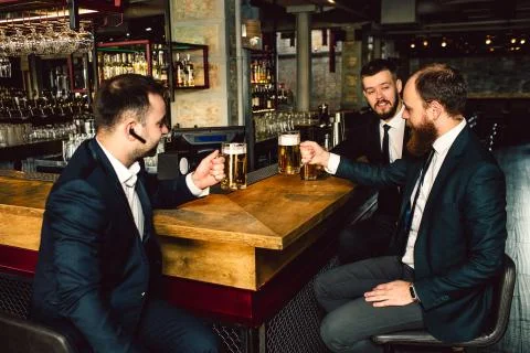 Three young businessman sit at table and hold cips of beer. They talk. People Stock Photos
