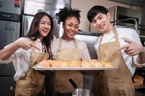 Three young chefs with baking bread, smile and are cheerful in the kitchen. Stock Photos