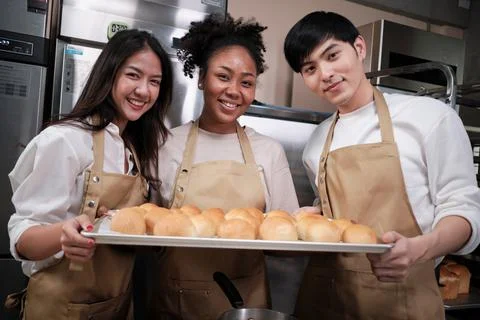 Three young chefs with baking bread, smile and are cheerful in the kitchen. Stock Photos