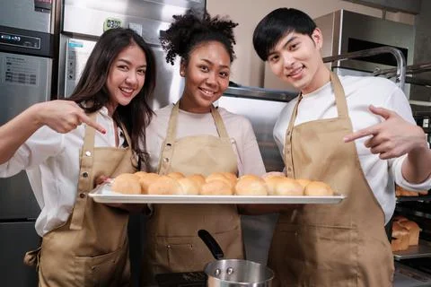 Three young chefs with baking bread, smile and are cheerful in the kitchen. Stock Photos
