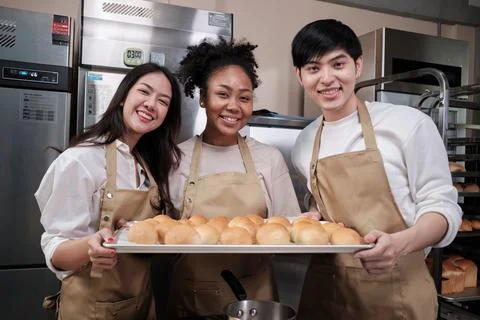 Three young chefs with baking bread, smile and are cheerful in the kitchen. Stock Photos