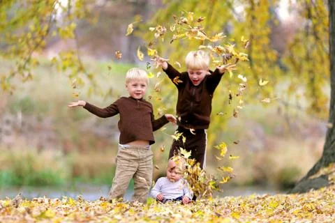 Three Young Children playing in Fallen Leaves Stock Photos