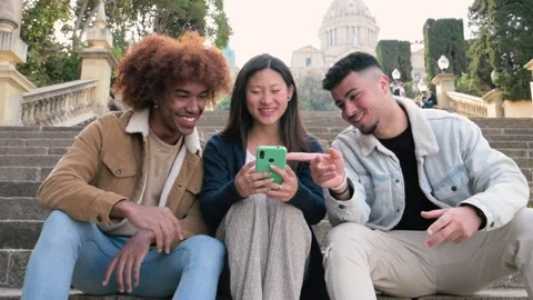 Three young diverse people looking at a smartphone sitting on the stairs.Two Stock Footage 247553904