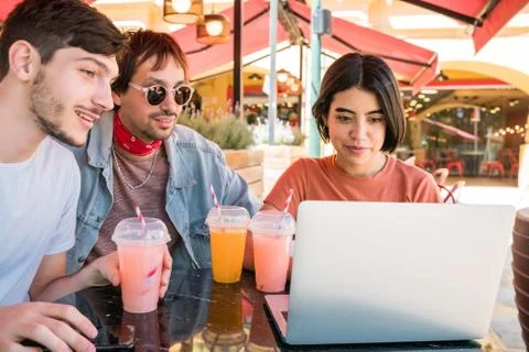 Three young friends using laptop at coffee shop. Stock Photos