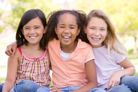 Three young girl friends sitting outdoors smiling Stock Photos