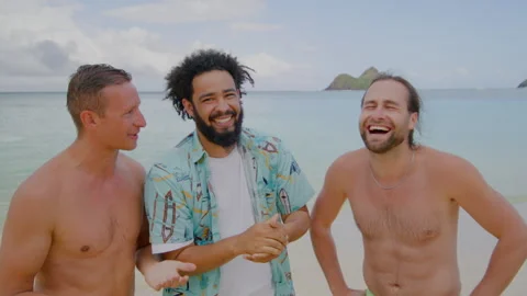 Three young guys laughing at the beach, enjoying water, sky, and fun times at Stock Footage 264995751