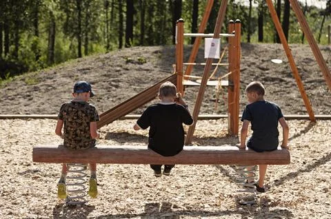 Three young guys sit on a bench supported by springs and talk Stock Photos
