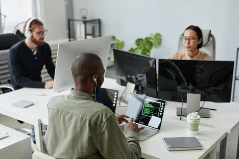 Three young intercultural diversity programmers sitting by computers Stock-Fotos