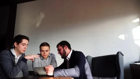 Three young male programmers communicate using tablet while sitting at desk in Video stock 78478990