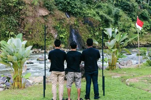 Three young men observing nature near flowing river waterfall Stock Photos