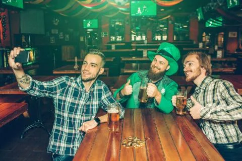Three young men sit at table in pub and take selfie. They pose on camera and Stockfoto's