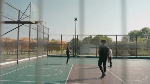 Three young men throwing basketball ball on a court in park on a sunny day Video stock 166835067