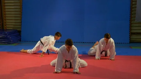Three young men wearing karate kimonos doing stretching exercises at the gym Stock Footage 76535456